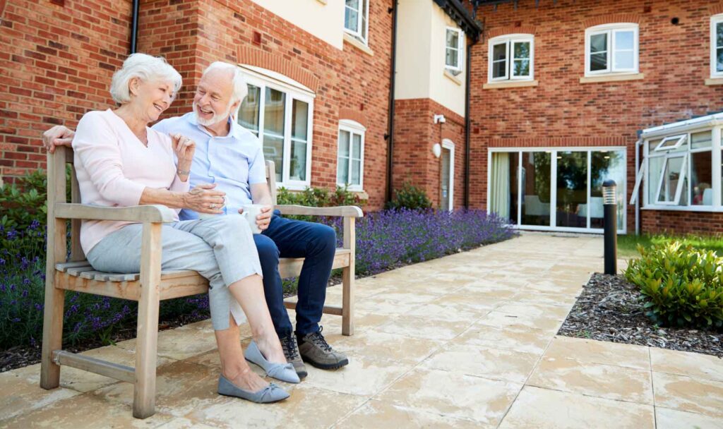 Two senior citizens sitting on a bench outside an apartment building